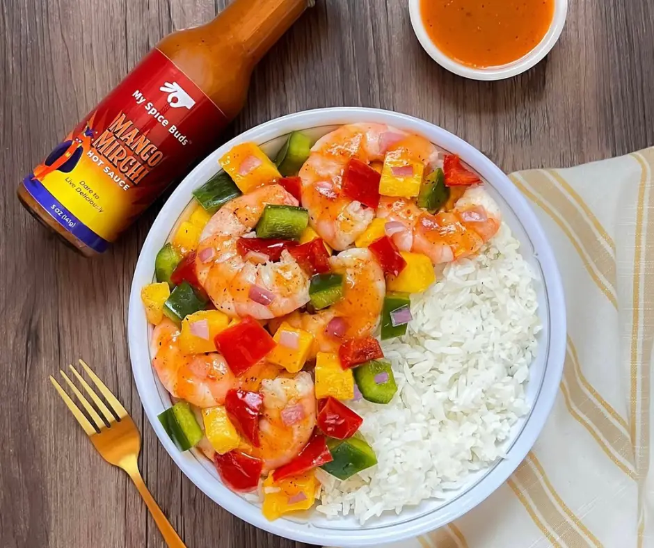 Shrimp and vegetable bowl with a bottle of sauce on a wooden table