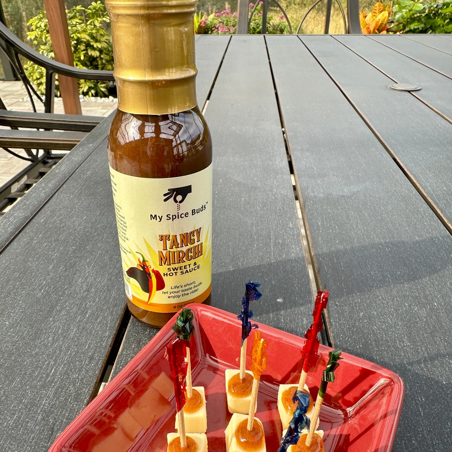 Bottle of 'My Spice Route' sauce with cheese bites on a red plate outdoors.
